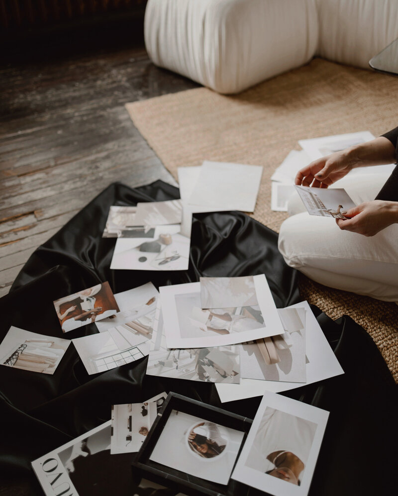 Creative collaboration and brand vision session—person sitting on a jute rug, curating design inspiration and brand imagery on black satin fabric. Surrounded by a modern white couch and rustic wood floor, the scene reflects Sable & Rose’s approach to partnering with clients to craft thoughtful, customer-focused brand identities driven by creativity and collaboration.