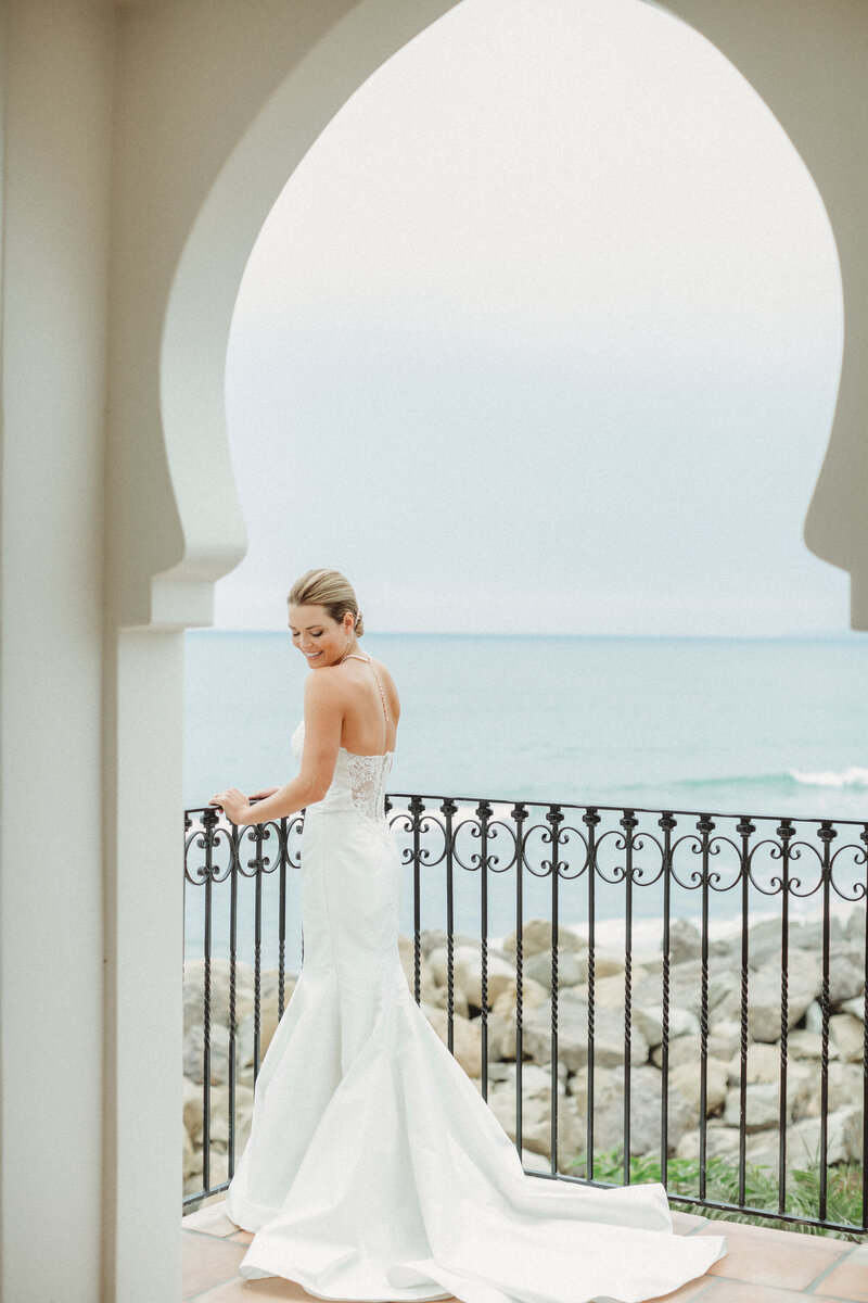 Bride wears her wedding gown and stands on balcony on her wedding day