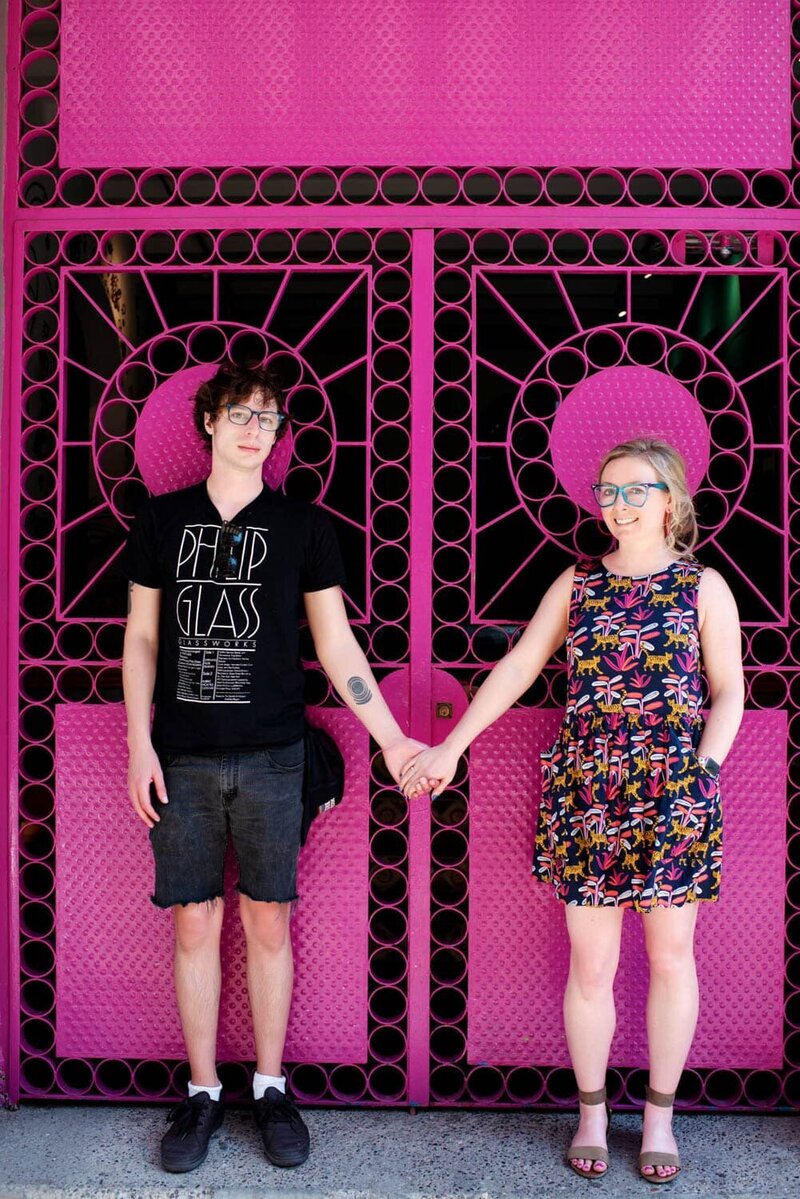 crystal genes photography holds hands with her boyfriend in front of a colorful pink doorway in puerto vallarta