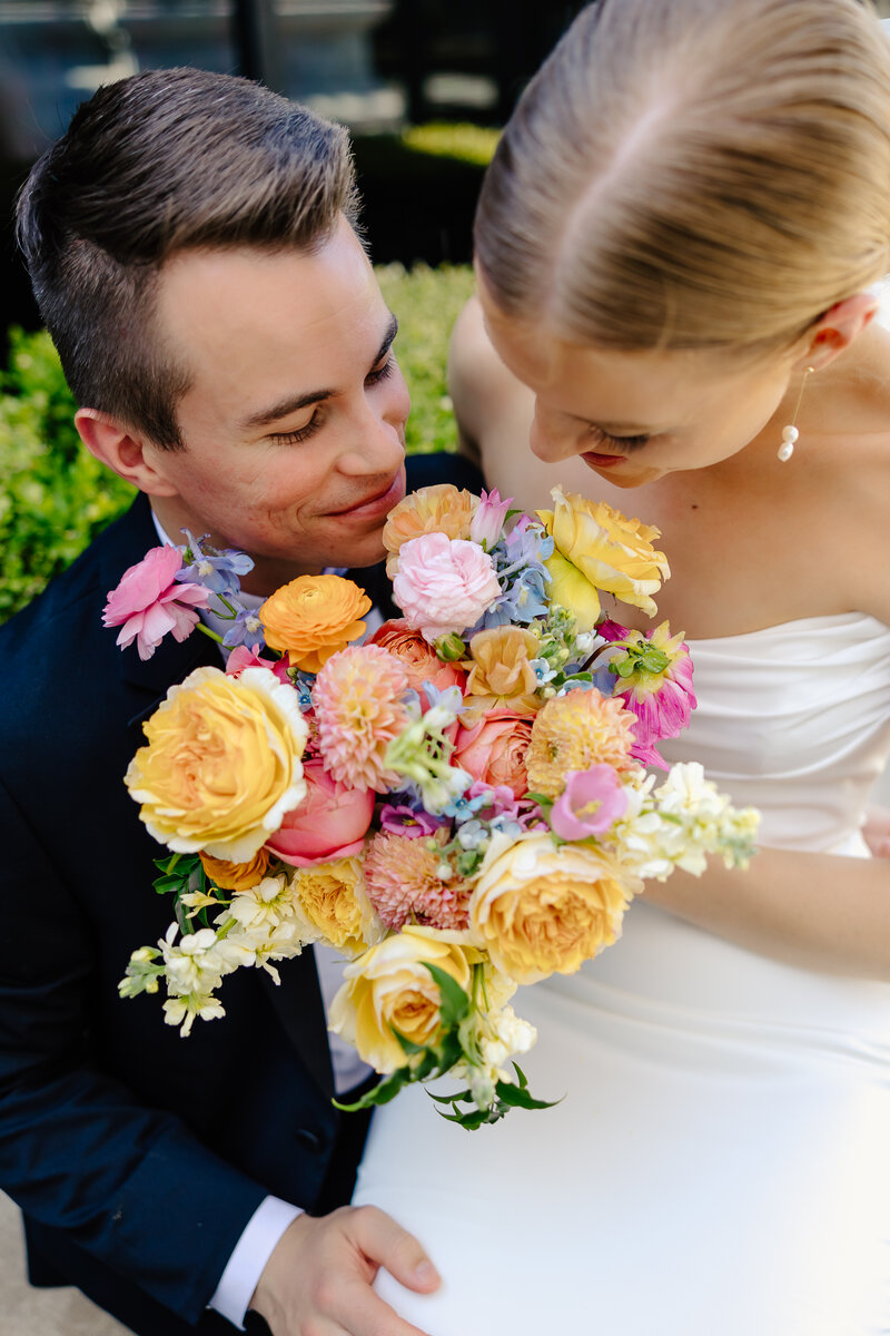 The following image shows a bride and groom enjoying the smell of the colorful bridal bouquet. It supplements the adjacent text that explains the Wichita KS wedding day. Photographed by Samantha Mudd Photo LLC, a professional wedding and lifestyle photographer based in Kansas City Missouri. Samantha is also a destination wedding photographer who will travel to wherever her clients take her.