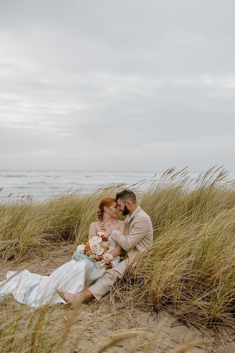 Couple sits among the sand dunes during their Oregon Coast elopement.