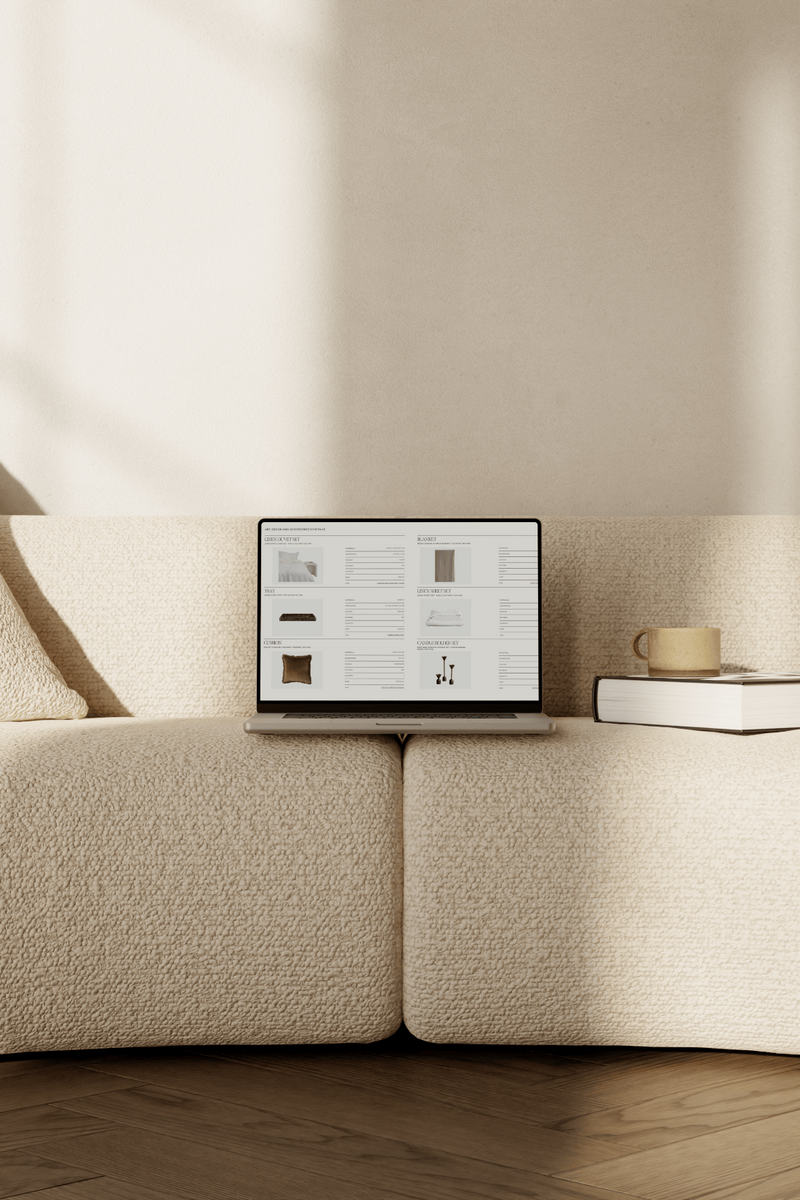 A laptop sits atop a sculptural cream bouclé sofa, its screen displaying the meticulously curated Art, Décor & Accessories Schedule for a Virtual Interior Styling project.