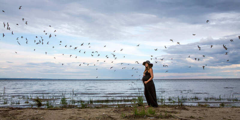 expectant mom on beach with birds flying by