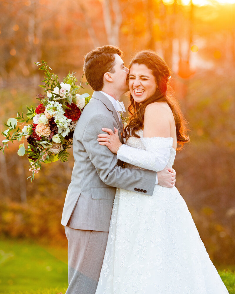 Bride laughs as the groom whispers in her ear during a New Hampshire vineyard wedding.