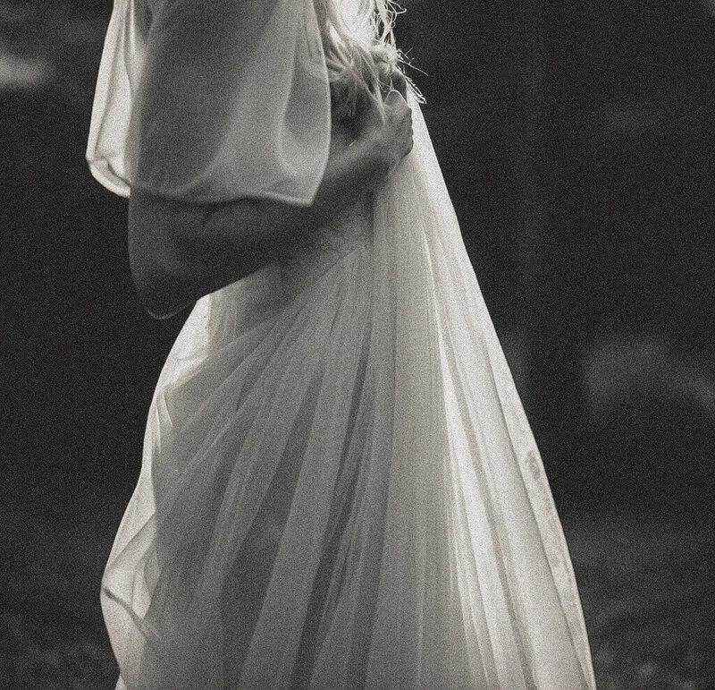 A person in a sheer, flowing dress holds the fabric at their waist. The image, created by Sweet Pea Ink Creative, is in black and white with soft, diffused lighting.