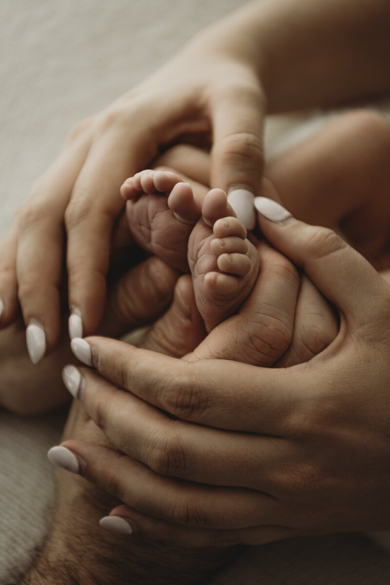 Close-up of adult hands gently cradling the tiny feet of a newborn baby.