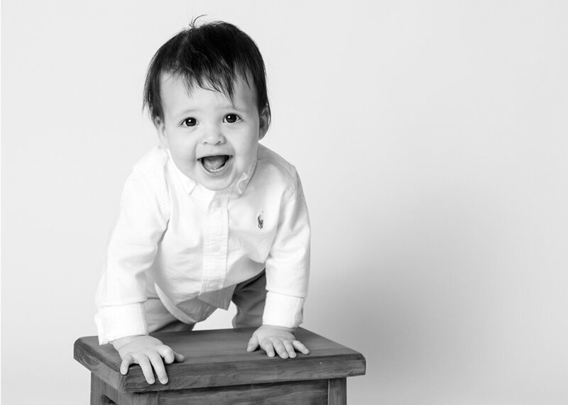 Black and white portrait of young boy wearing white shirt and smiling while leaning on stool