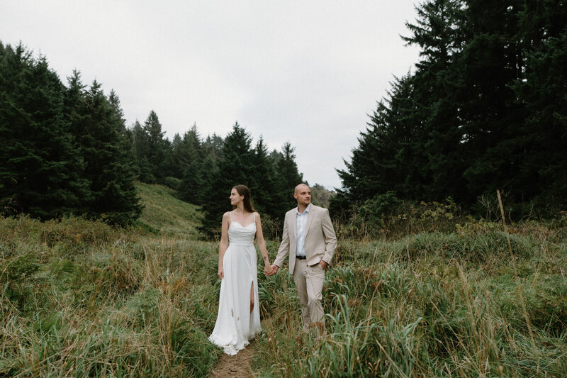 A couple stands in the grass against dramatic skies during their Cannon Beach elopement. 