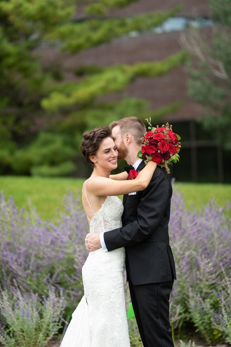 Bride and groom embrace while holding red roses bouquet