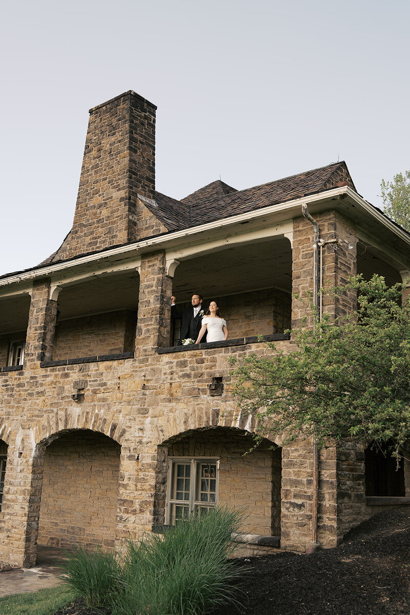 bride and groom lookin gout large stone window on their wedding day 