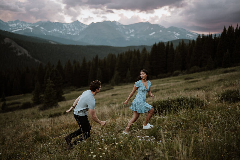 Playful couple runs through wildflower meadow in Breckenridge, Colorado mountains at sunset.