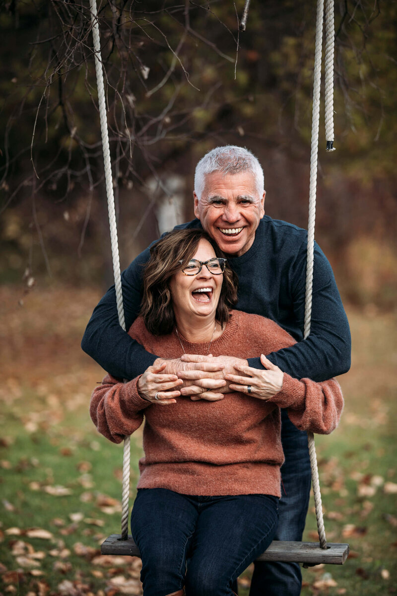 couple laughs and hugs on a swing