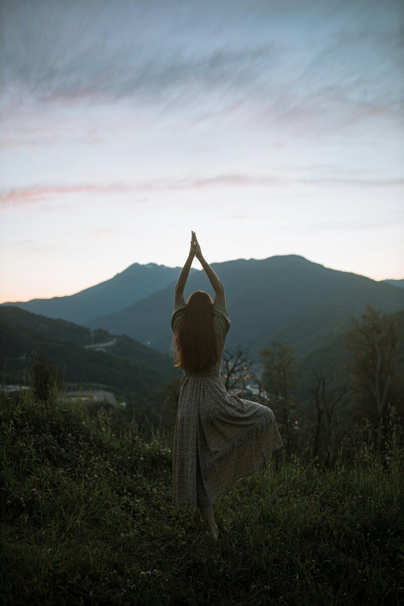 Nicole practicing yoga on a mountain hillside at sunrise, embodying wellness and soulful travel.