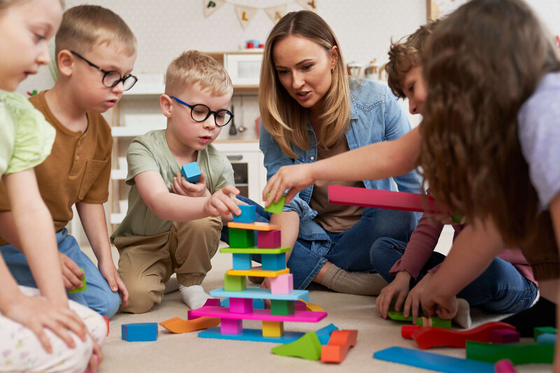 teacher assisting a group of kids playing with colorful blocks