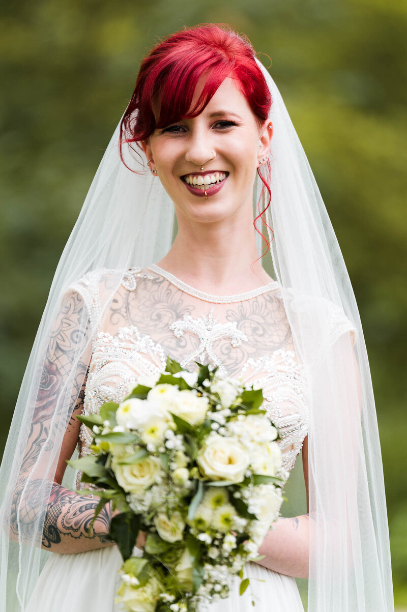 Braut mit Roten Haar hält Brautstrauß und lächelt in die Kamera bei Hochzeit