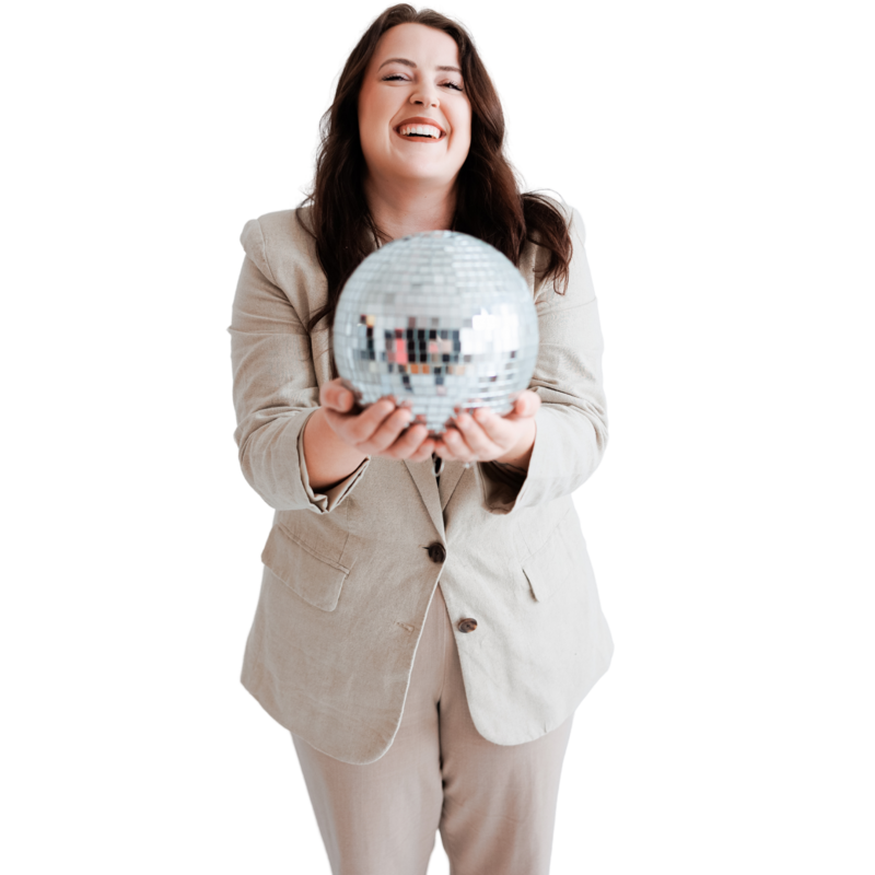 This is a picture of Mariah of Moonlight Design holding a disco ball and laughing. She is wearing a tan suit. 