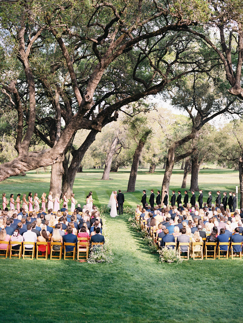 Photo from far back of an outdoor wedding ceremony under trees