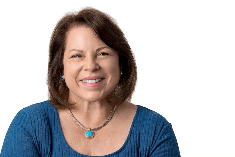 woman wearing a blue blouse smiling at the camera with a white backdrop