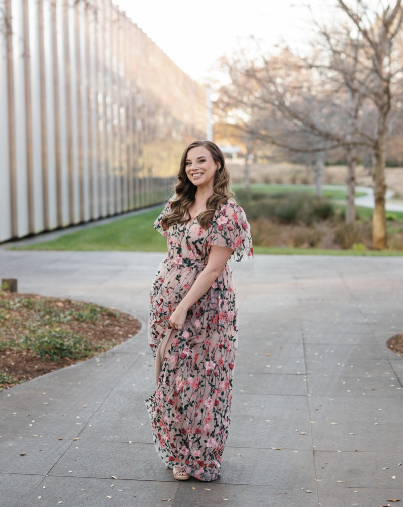 Portrait of Brandie Baird, Raleigh & Wilmington wedding photographer, standing in a floral dress, smiling warmly.