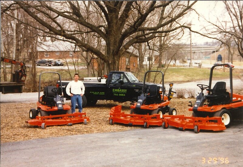 archive photo of Embassy Landscape founder in front of a black work truck and three riding lawnmowers from the 80s