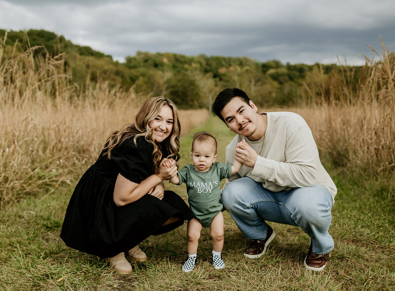 mom and dad on the ground outside while holding baby in the middle