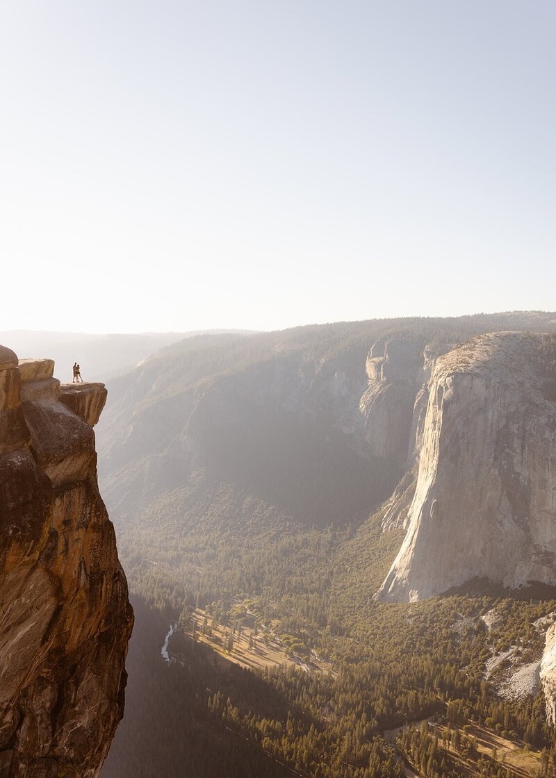 Couple holding each other and kissing on the cliff of Taft Point with El Capitan and Yosemite Valley in view