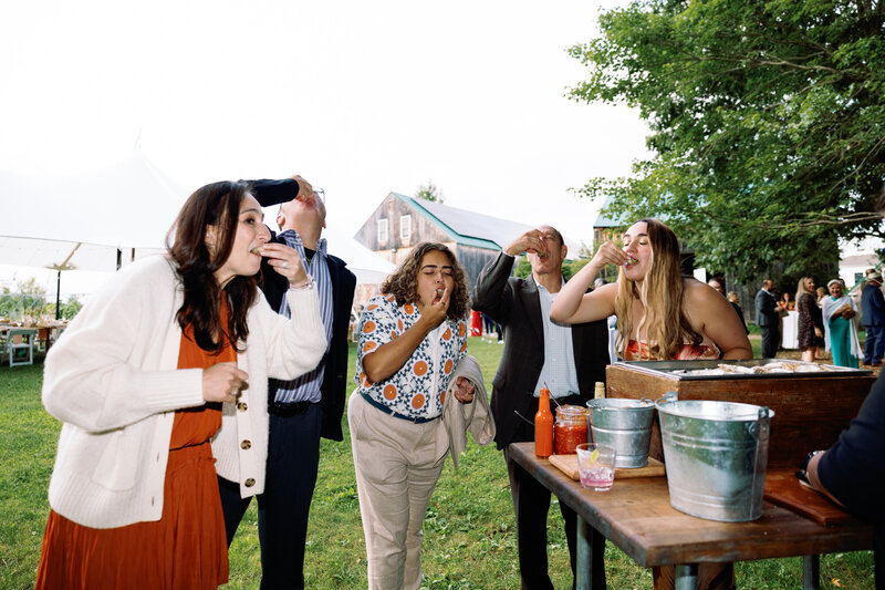 bright fun photo of guests eating oysters at raw bar at new england barn wedding 
