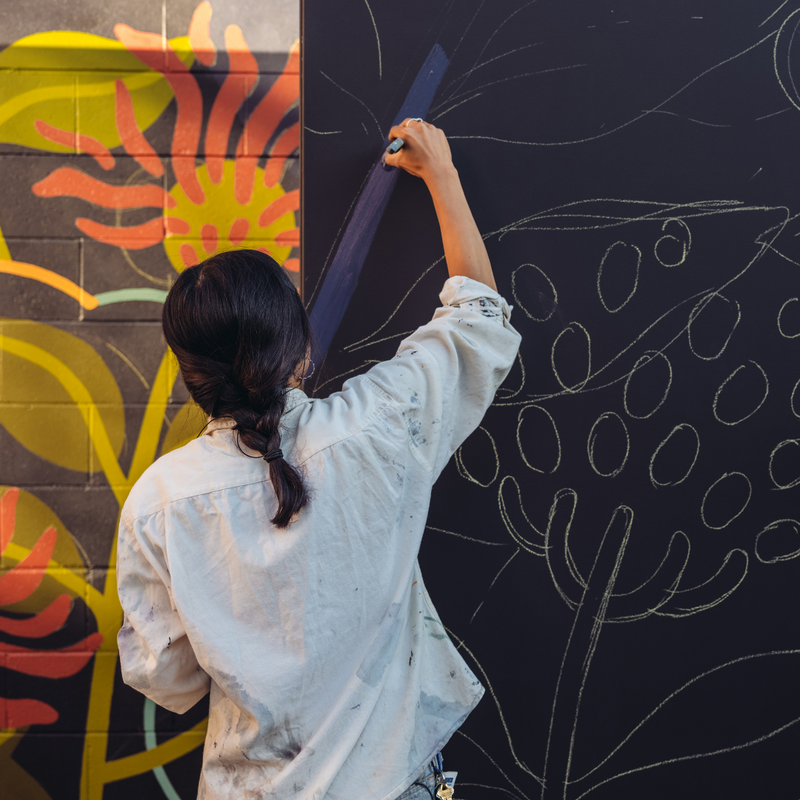 Woman is standing and painting a floral mural