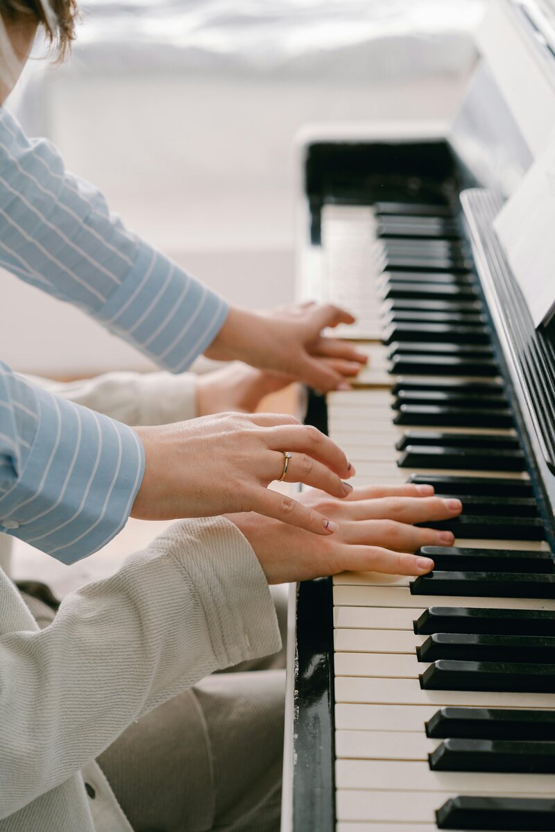 Child playing the piano with the instructor guiding their hands.