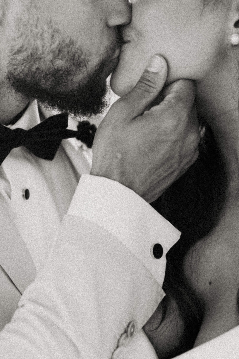 Romantic close-up of groom holding bride’s chin as they share a kiss during their intimate Santorini elopement.