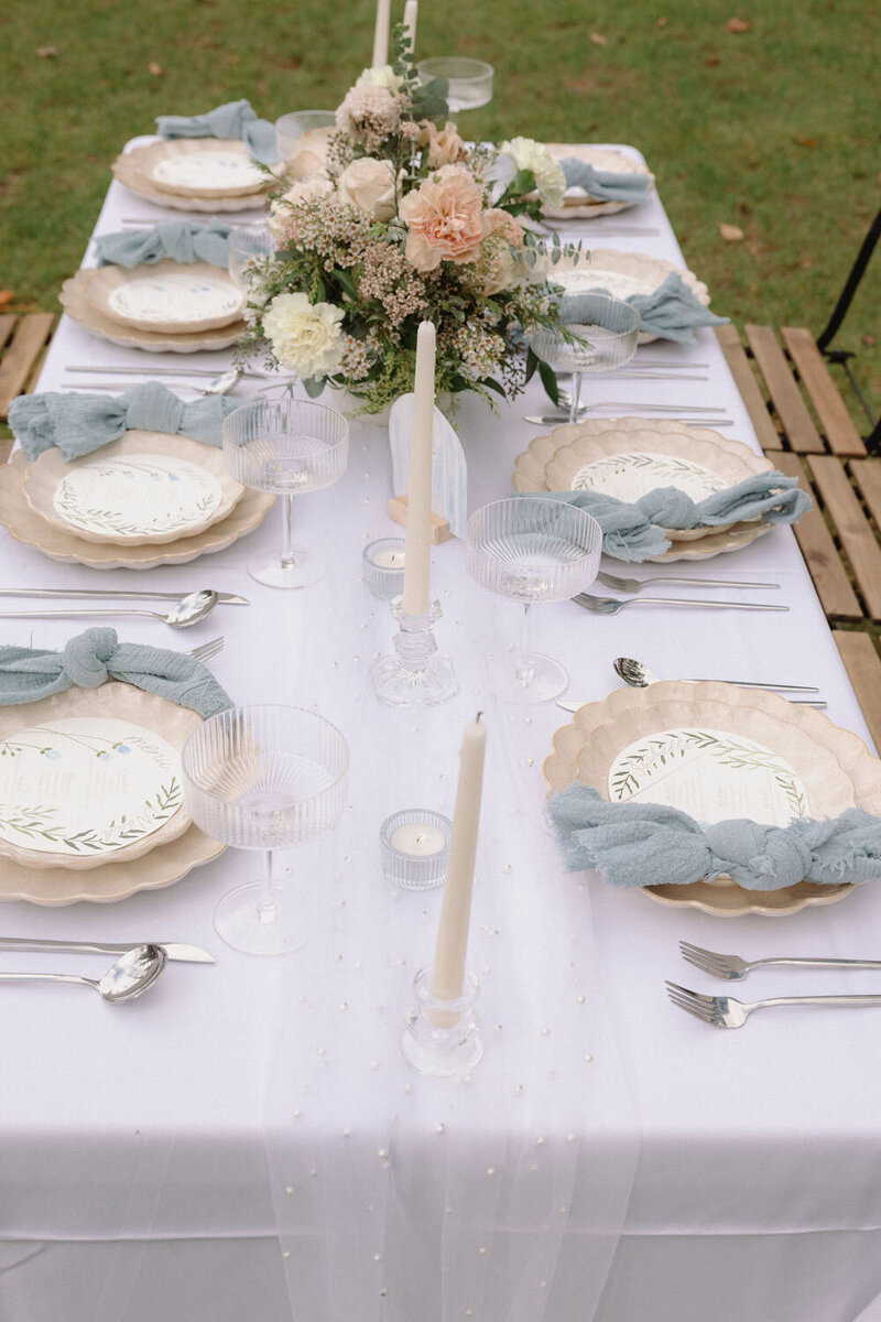 Outdoor tablescape with blue linens, floral centerpiece, and candles