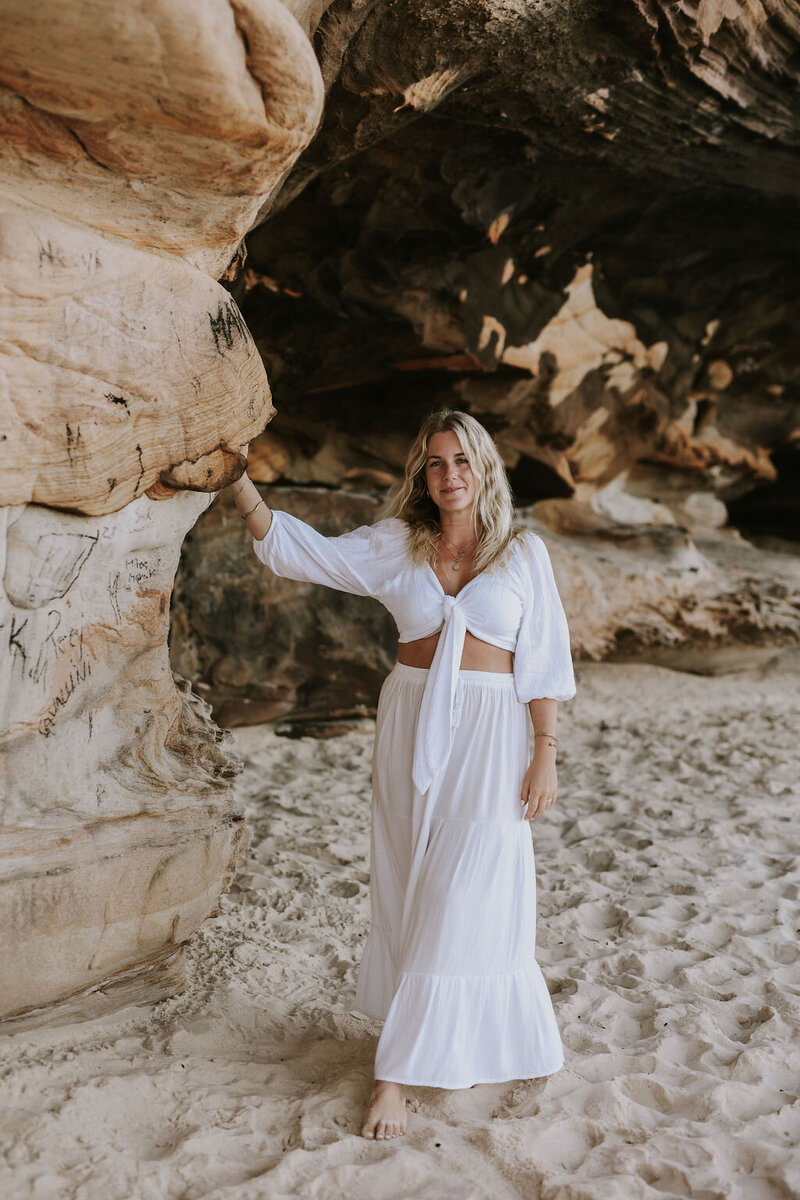 Photo of woman standing next to a cliff on the beach 