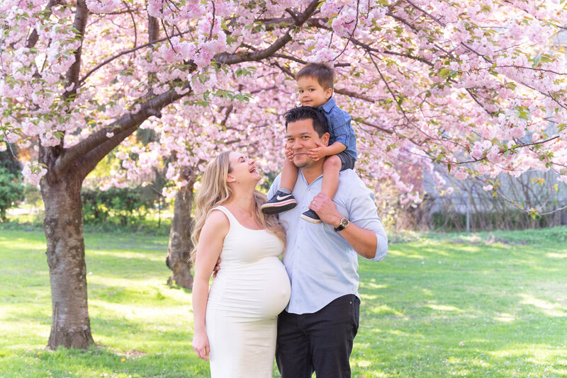 A pregnant woman laughing with her husband and her son.