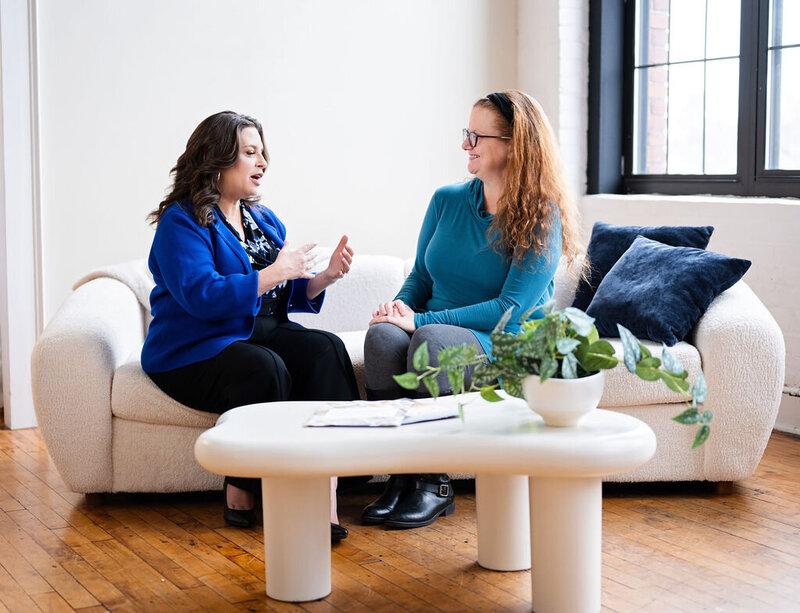 Back view of Chris walking outdoors in a tan coat, showcasing her long wavy brown hair.