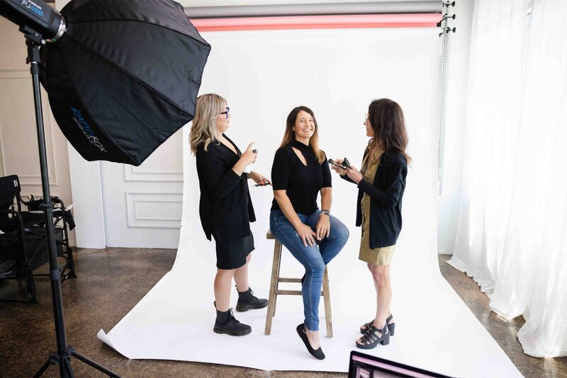 Behind the scenes of professional brand photoshoot showing creative team preparing client in studio setting with lighting equipment and white backdrop