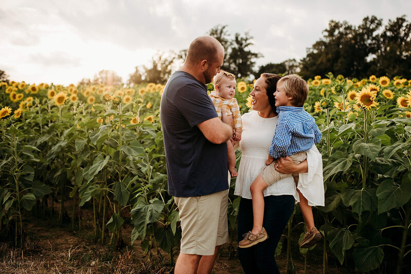 Mother and Father holding boy and girl in summer clothing at a sunflower field in Jarrettsville Maryland