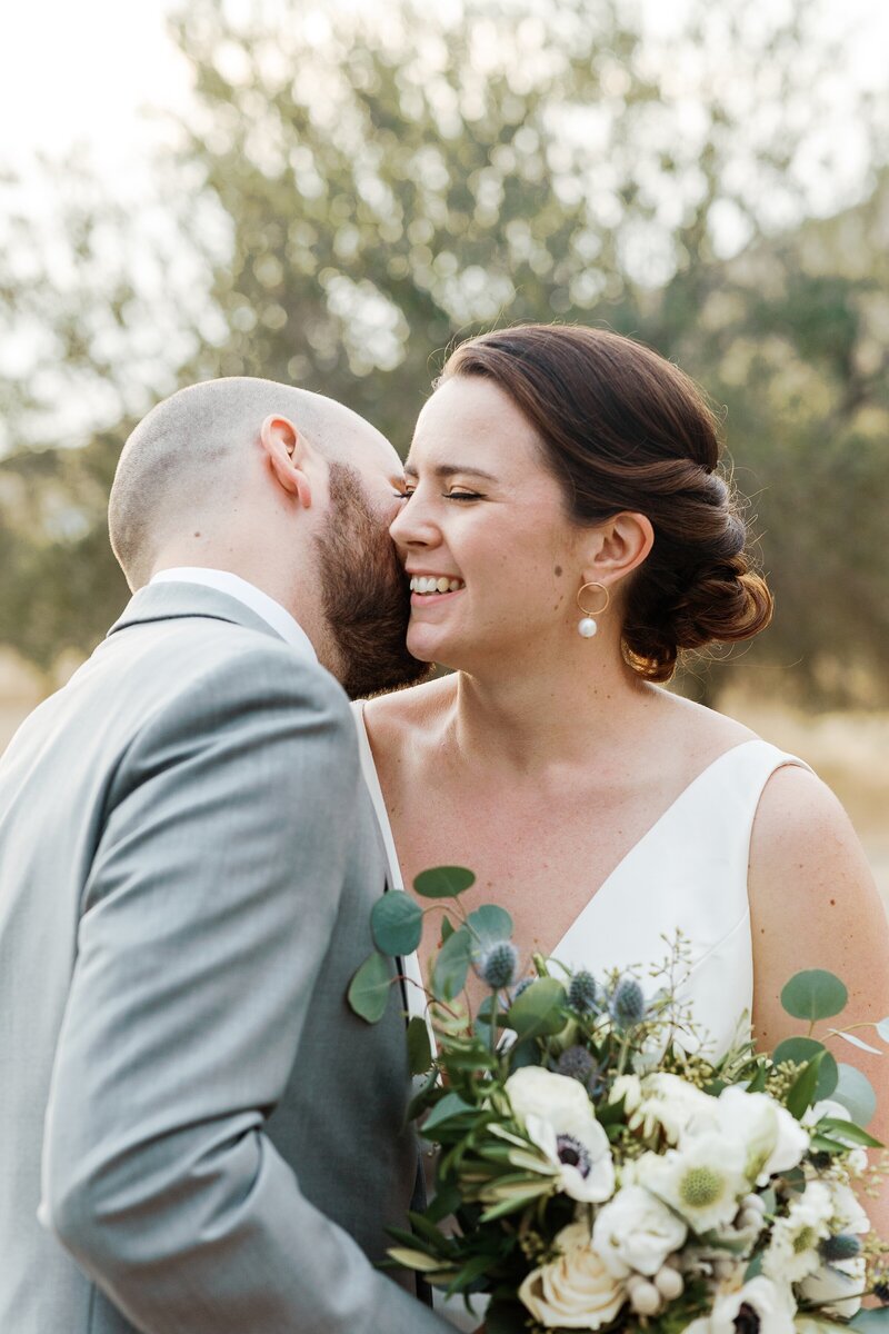 Groom kisses brides cheek making her laugh