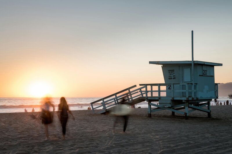 California beach lifeguard tower at sunset with people walking along the shore
