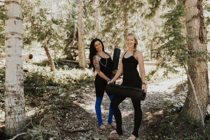 two women smiling standing in the woods with yoga mats