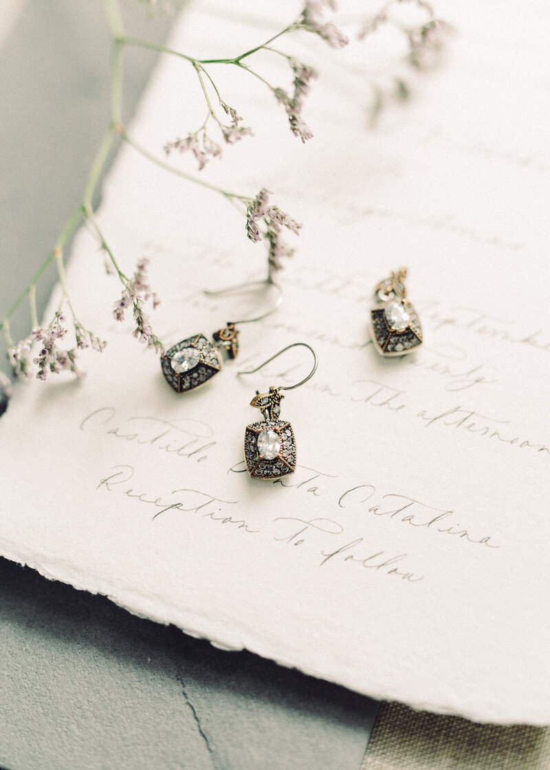 Close up of brass and diamond earrings sitting on paper with calligraphy writing