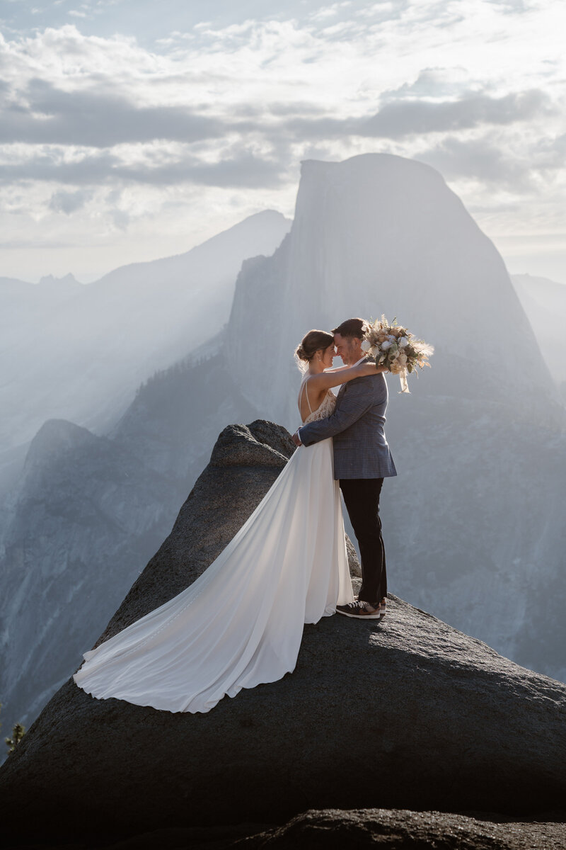 A couple holds each other in wedding attire before their elopement in front of Half Dome in Yosemite National Park