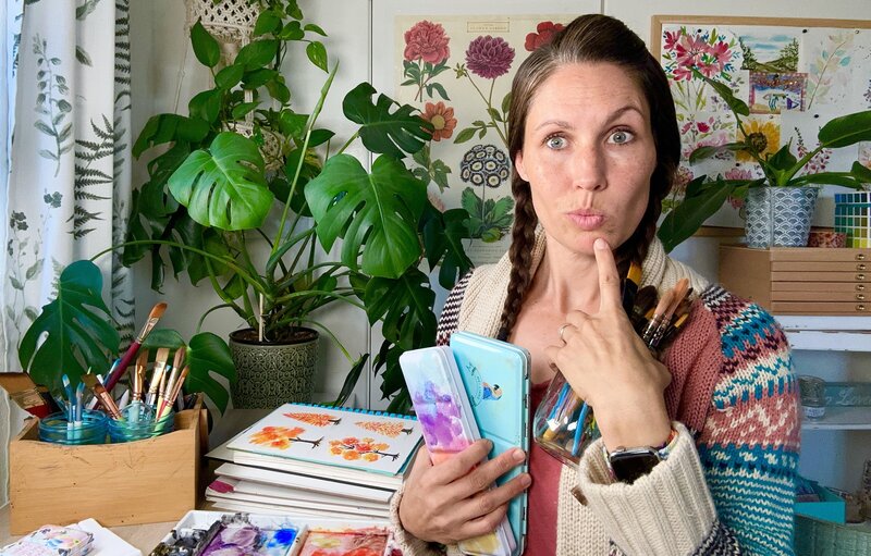 Woman with big eyes and finger on chin holding paint brushes and paint palette
