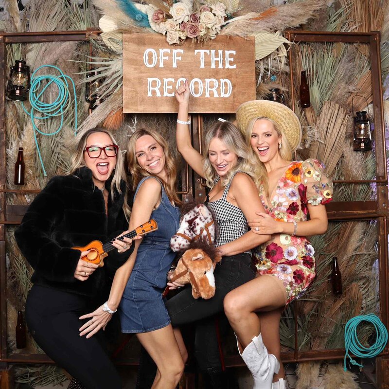 Group of women posing with playful props in front of a rustic western-themed backdrop and “Off The Record” sign, captured by MISGIF’s custom photo booth at a corporate or community event in Phoenix, Arizona