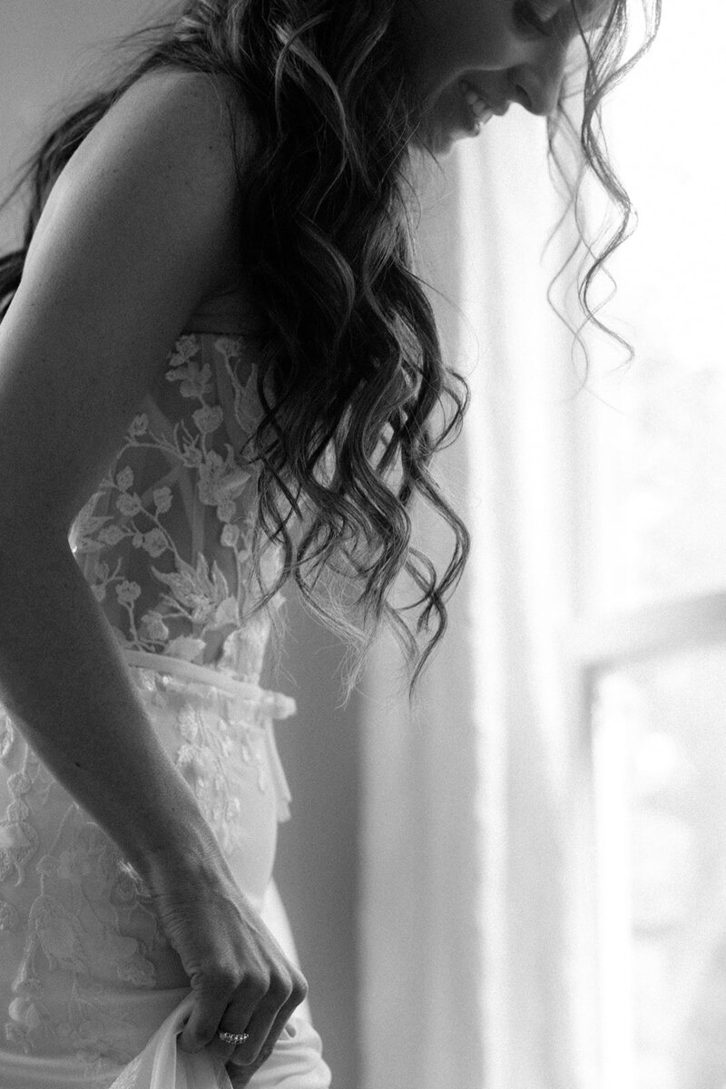 Bride smiles as she looks at her dress while getting ready in the bridal space at Cheekwood Gardens. 