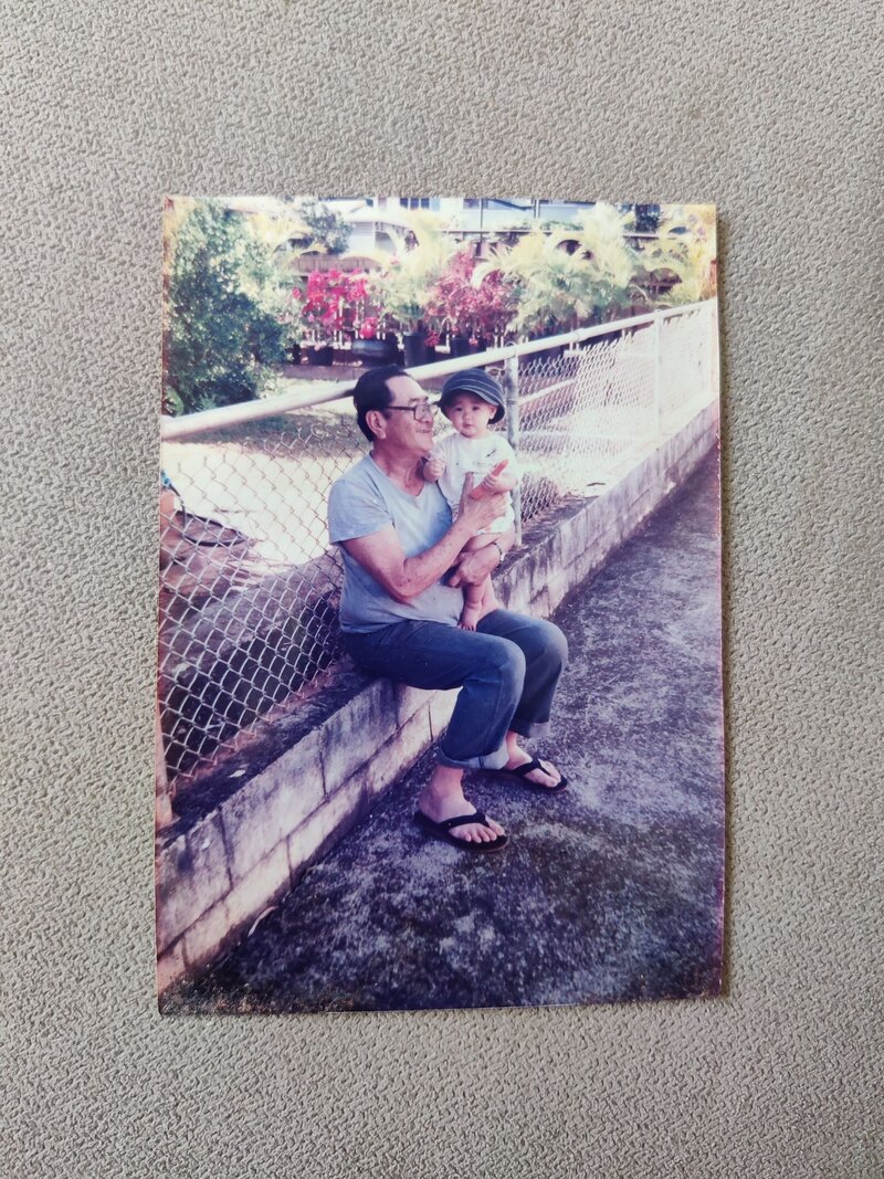 A grandfather sitting on the edge of a brick wall holding a small child 
