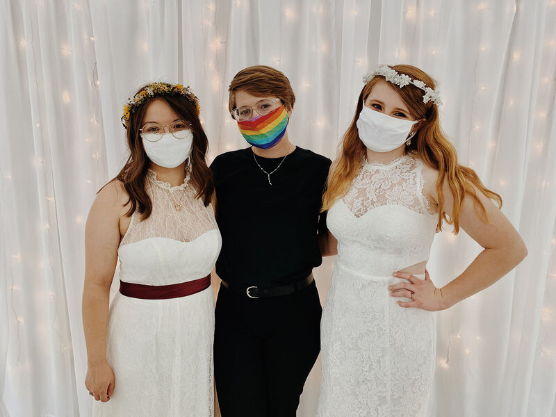 A Virginia elopement photographer wears a rainbow mask and stands in between two LGBTQ+ marriers wearing white masks on their wedding day in 2020.