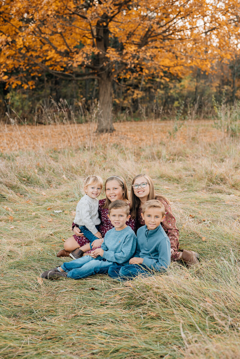 Siblings snuggle close together near autumn trees.
