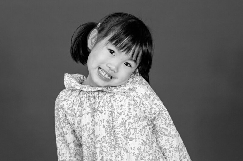 Black and white image of girl her head is leaning on one sholder and she has a big smile on her face for phootos
