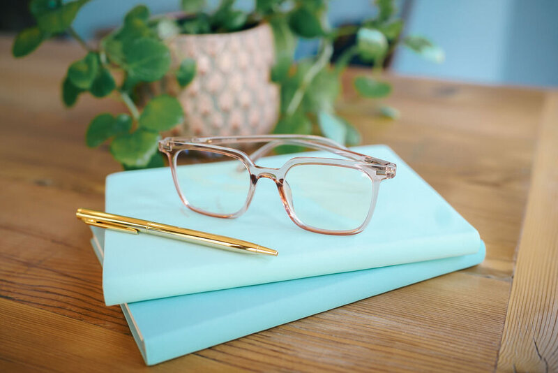 Pink glasses and a gold pen resting on top of green journals.