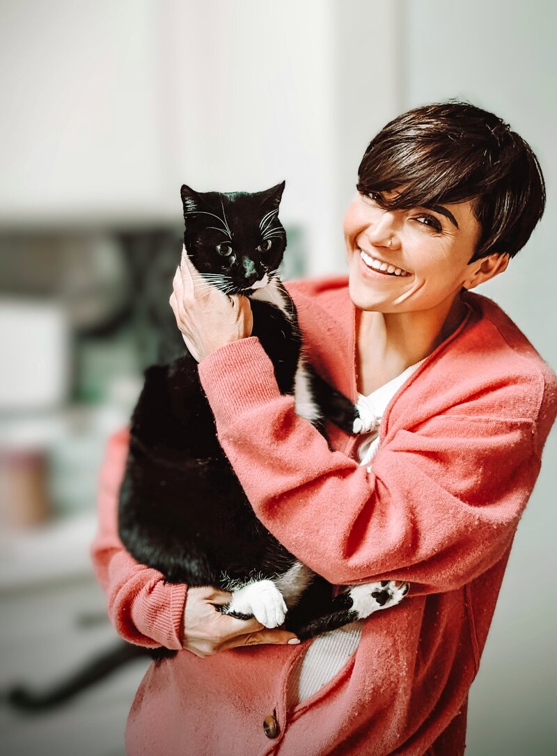 Brunette in pastel pink cardiga, holding her black and white cat